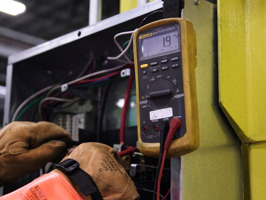 Technicien ganté relevant une mesure au multimètre sur un équipement électrique