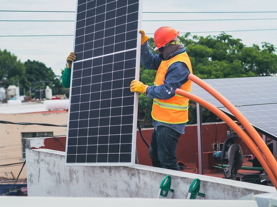 Technicien installant un panneau solaire sur la toiture d’un bâtiment, dans une ville tropicale